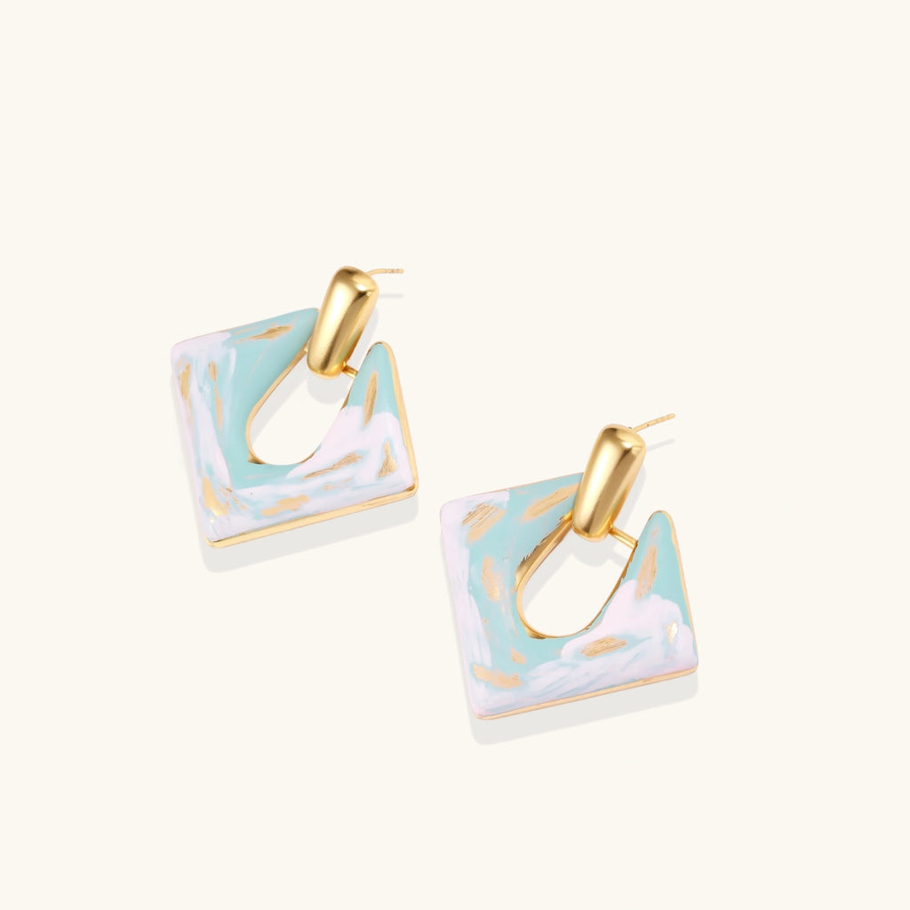 Geometric square enamel earrings with marbled turquoise and lavender pattern, gold U-shaped connector on cream background.